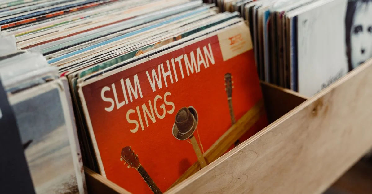 Disques vinyles assortis dans une caisse en bois mettant en avant l'album 'Slim Whitman Sings'.