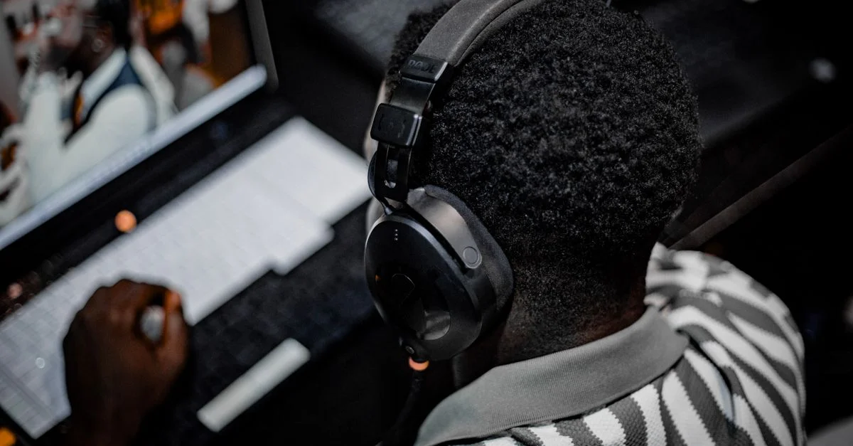 Un homme utilise un ordinateur portable et un casque audio, travaillant intensément dans un environnement intérieur.