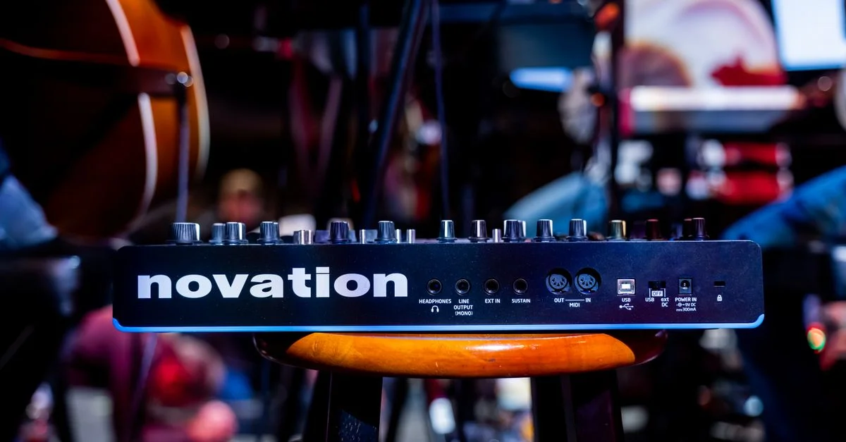 Dispositif audio Novation sur un tabouret lors d'un setup de concert en direct, mettant en avant la technologie musicale.